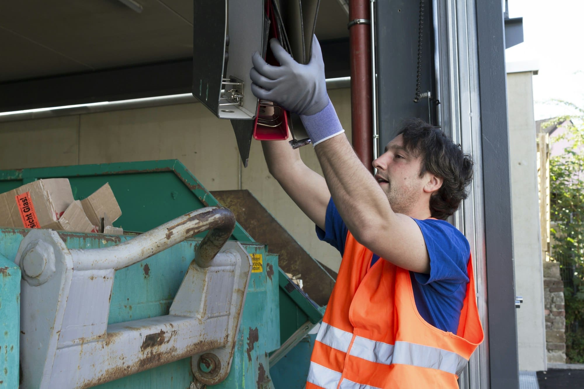 Worker at a waste container throwing away folders